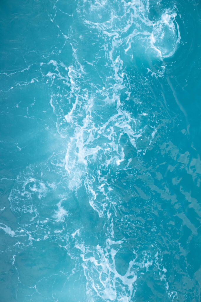 Top-down view of turquoise ocean waves and foam swirling in the water